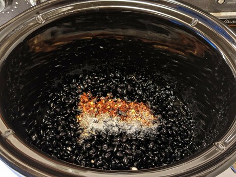 Beans and spices in a black ceramic slow cooker insert, awaiting water, time, and heat.