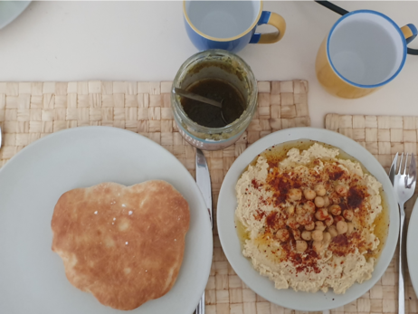 a pita, hummus on separate plates and zhug in the jar