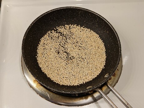 Smol nonstick frying pan just barely filled with a single layer of white sesame seeds, being dry toasted.