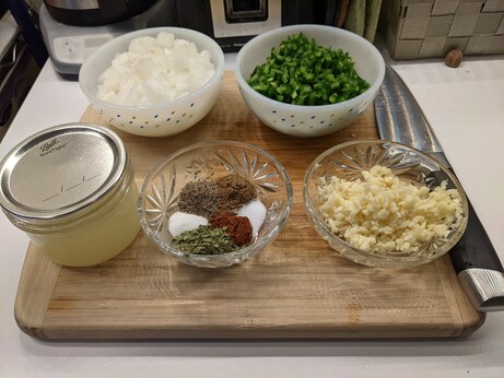 Ingredients now prepped: five bowls, top left full of finely diced white onions, top right full of finely diced seeded and de-ribbed jalapeños, front right full of diced garlic, middle center with the spices again, and a short mason jar on the bottom left about 2/3 of the way full of freshly squeezed lime juice.