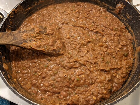 Brick brown pinto beans now added to the vegetables and spices, at this point roughly mashed - there is still a lot of visible texture.