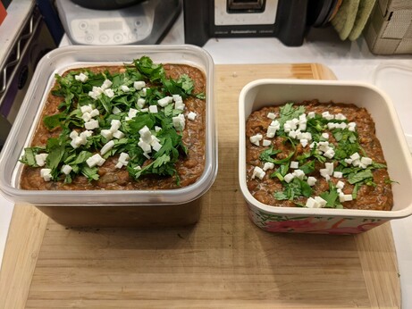 Two large square fridge dishes full of beans, topped with chopped cilantro and diced feta.